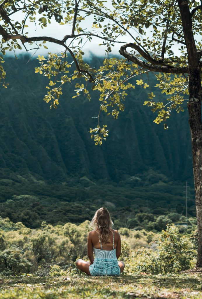 Unrecognizable female meditating on grass in highlands on sunny day